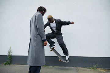 Gen Z black boy shows skateboard moves on sidewalk to his friend © Ejatu Shaw