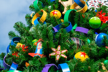 A tall outdoor Christmas tree with lush green fir branches, plastic ribbon circle garland, colorful...