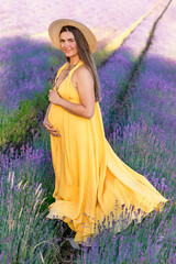 A pregnant woman in a yellow dress stands on a blooming lavender field
