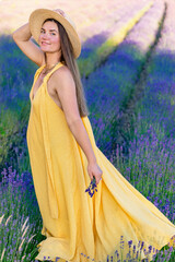 A pregnant woman in a yellow dress stands on a blooming lavender field