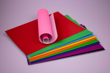 A roll of pink corrugated paper on multicolored leaves of corrugated paper