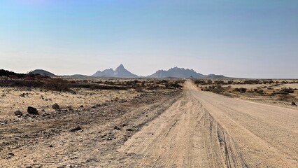 Endless gravel road. Spitzkoppe in a distance. Blue sky without clouds