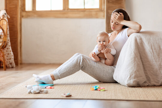 Depressed young woman sitting with cute baby boy on floor