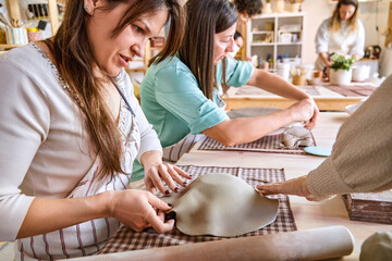 Woman molding and shaping clay while making crafts in a pottery class. Craft and hobby concept.