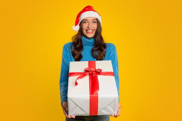 Happy woman poses with wrapped gift box on yellow background
