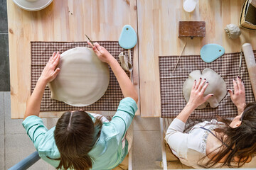 Top view of two women working with clay while creating craft pieces in a pottery class. Craft and...