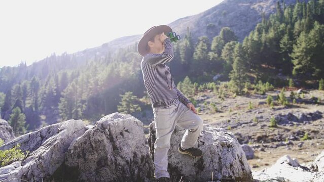 Boy kid little tourist boy with binoculars in forest and the mountains