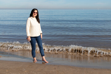 black-haired girl walking along the beach shore in autumn with bare feet
