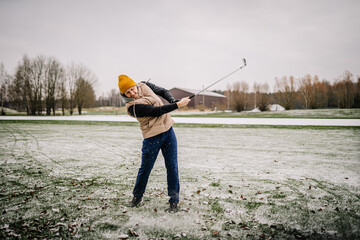 A man makes a shot with a club on the golf course in winter