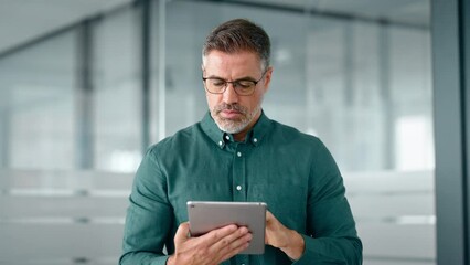 Smiling busy middle aged business man investor using tablet computer, mature older businessman executive manager looking at tab satisfied with finance trading market working standing in office. - Powered by Adobe