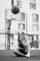 a basketball player in sportswear is sitting while smiling and throwing the ball