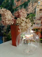 transparent glass candy bowl in a pumpkin shape on the kitchen table with flowers in a vase.