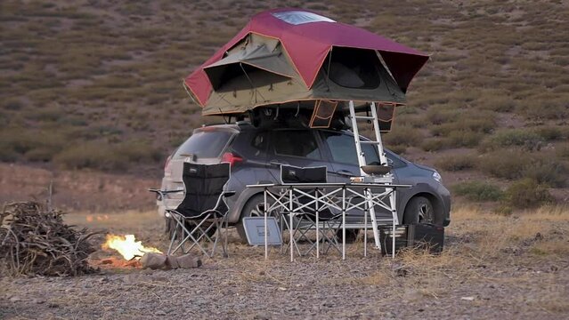 Desert camping, with an SUV equipped with a roof tent and foldable table and chairs mounted behind a fireplace
