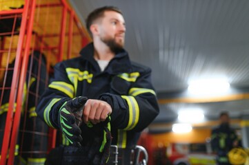 Fireman putting on protective uniform and preparing for action while standing in fire station