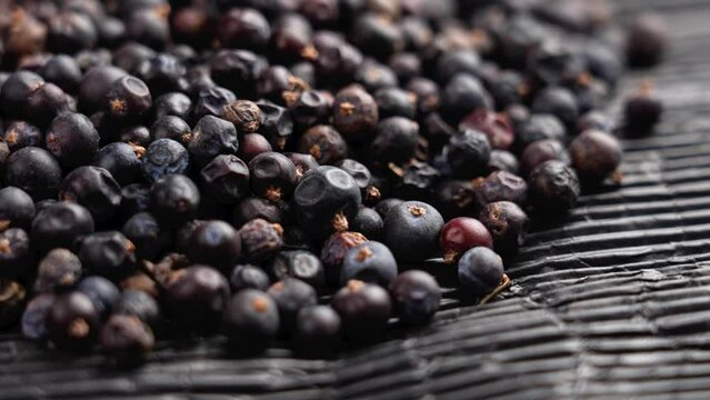 Dried juniper berries on a black paper. Dehydrated aromatic medicative ingredient. Rotation. Macro shot