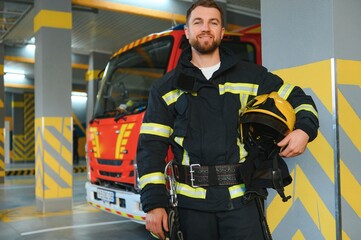 Fototapeta premium Firefighters man in a protective suit near fire truck. Protection, rescue from danger. Fire station