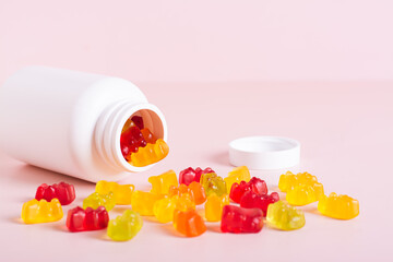Chewable vitamin supplements spilled from a bottle on a pink background