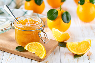 Sweet orange jam in jar with juicy orange slices on wooden table.