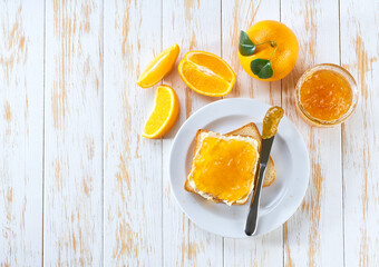 toast with orange jam, jar of jam, knife on a light wooden table. view from above