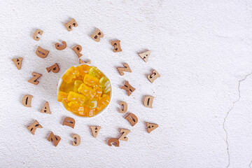 Chewable multivitamins in the form of candy bears in a bowl and wooden letters top view