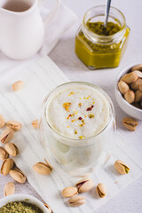 Pistachio matcha latte in a cup and nuts in a bowl and on the table vertical view