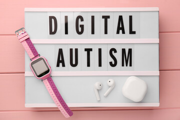 Lightbox with phrase Digital Autism, smartwatch and earphones on pink wooden table, top view