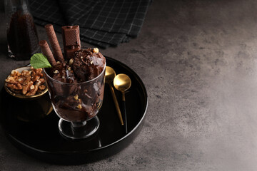 Tasty chocolate ice cream with sauce, nuts and wafer rolls in glass dessert bowl on dark grey table. Space for text