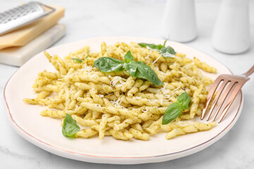 Plate of delicious trofie pasta with pesto sauce, cheese and basil leaves on white marble table