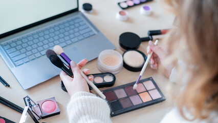 A faceless woman watches online training from a professional makeup artist on a laptop. Distance...