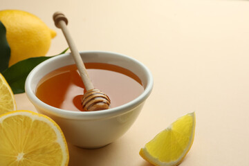 Ripe lemons, bowl of honey and dipper on beige background, closeup. Space for text