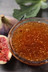 Bowl with tasty sweet jam and fresh figs on grey table, closeup