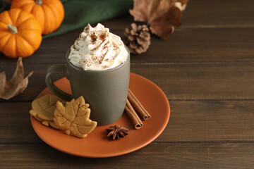 Tasty pumpkin spice latte with whipped cream in cup and cookies on wooden table. Space for text