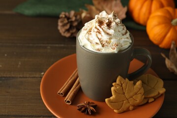 Tasty pumpkin spice latte with whipped cream in cup and cookies on wooden table, closeup
