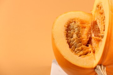 Cut fresh ripe pumpkin on pale orange background, closeup. Space for text