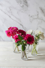 Bouquet of beautiful wild flowers and leaves in vases on white wooden table against marble background