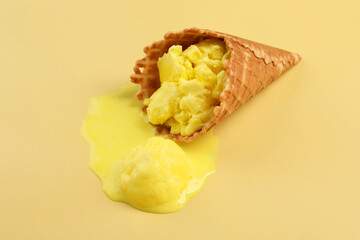 Melted ice cream in wafer cone on pale yellow background