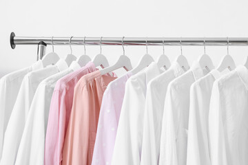 Rack with different stylish shirts near white wall, closeup. Organizing clothes