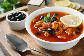Meat solyanka soup with sausages, olives, vegetables in bowl and spoon on grey table, closeup