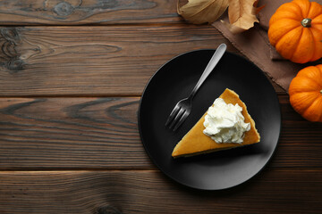 Piece of delicious pie with whipped cream, pumpkins and fork on wooden table, flat lay. Space for...