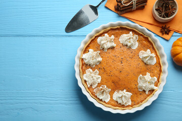 Delicious pumpkin pie with whipped cream and spices on light blue wooden table, flat lay. Space for text