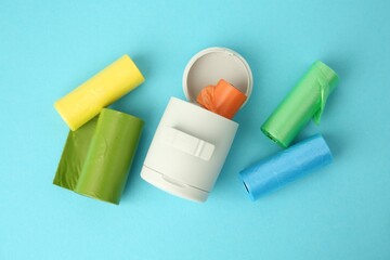 Dog waste bags and dispenser on light blue background, flat lay