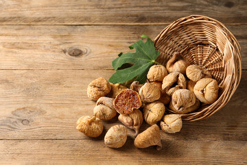 Overturned wicker basket, dried figs and green leaf on wooden table. Space for text
