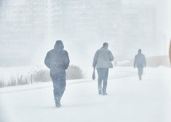 A snowstorm. People walk down the street during a snowstorm. Heavy snowfall. against the background of a cold urban landscape.