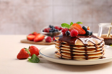 Stack of tasty pancakes with fresh berries, chocolate sauce and mint on white table. Space for text
