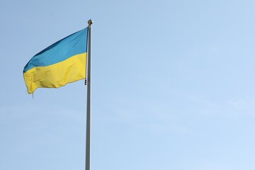 Flag of Ukraine waving on pole against blue sky. Space for text