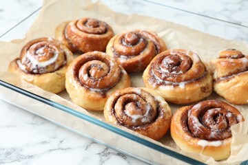 Baking dish with tasty cinnamon rolls on white marble table, closeup