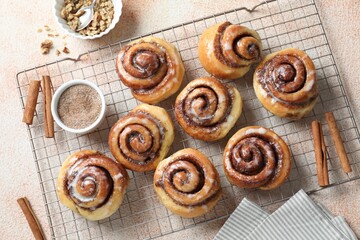 Tasty cinnamon rolls, sticks and nuts on beige textured table, flat lay
