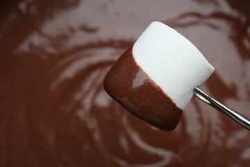 Marshmallow with melted chocolate on fork above fondue, closeup. Space for text