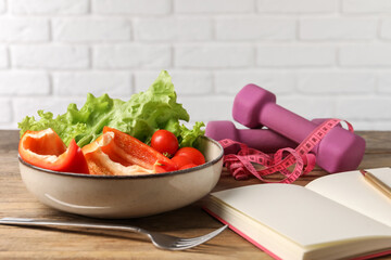 Healthy diet. Vegetables, fork, notebook, dumbbells and measuring tape on wooden table, closeup