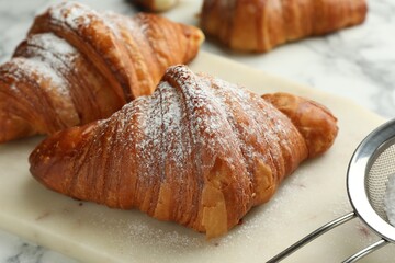 Tasty croissants with powdered sugar on white marble table, closeup